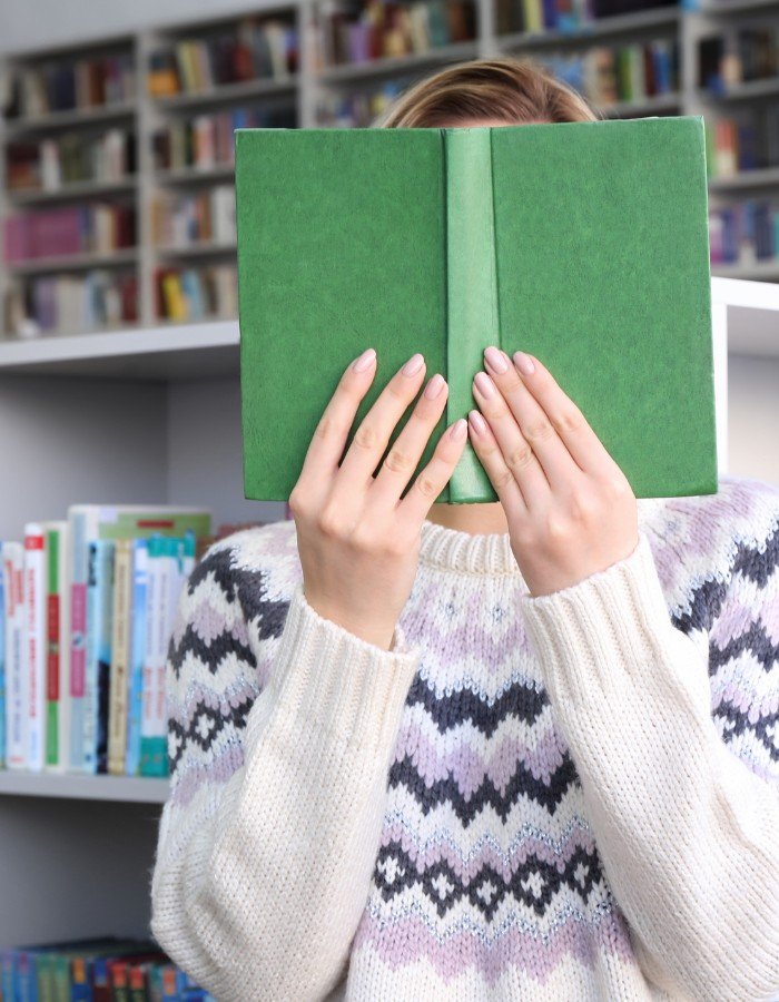 Faceless YouTube Channel A woman hiding her face with a book as a faceless YouTuber.